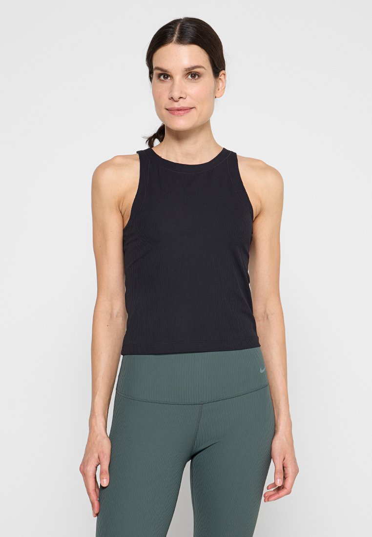 Schwarzes geripptes Tanktop mit rundem Ausschnitt und ärmellosem Design, kombiniert mit dunkelgrünen hochtaillierten Leggings. Glatte Stofftextur.
