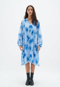 Hellblaues Kleid mit plissierter Optik, das blaue abstrahierte Muster aufweist. Lange Ärmel mit elastischen Bündchen und V-Ausschnitt. Knöchellang.