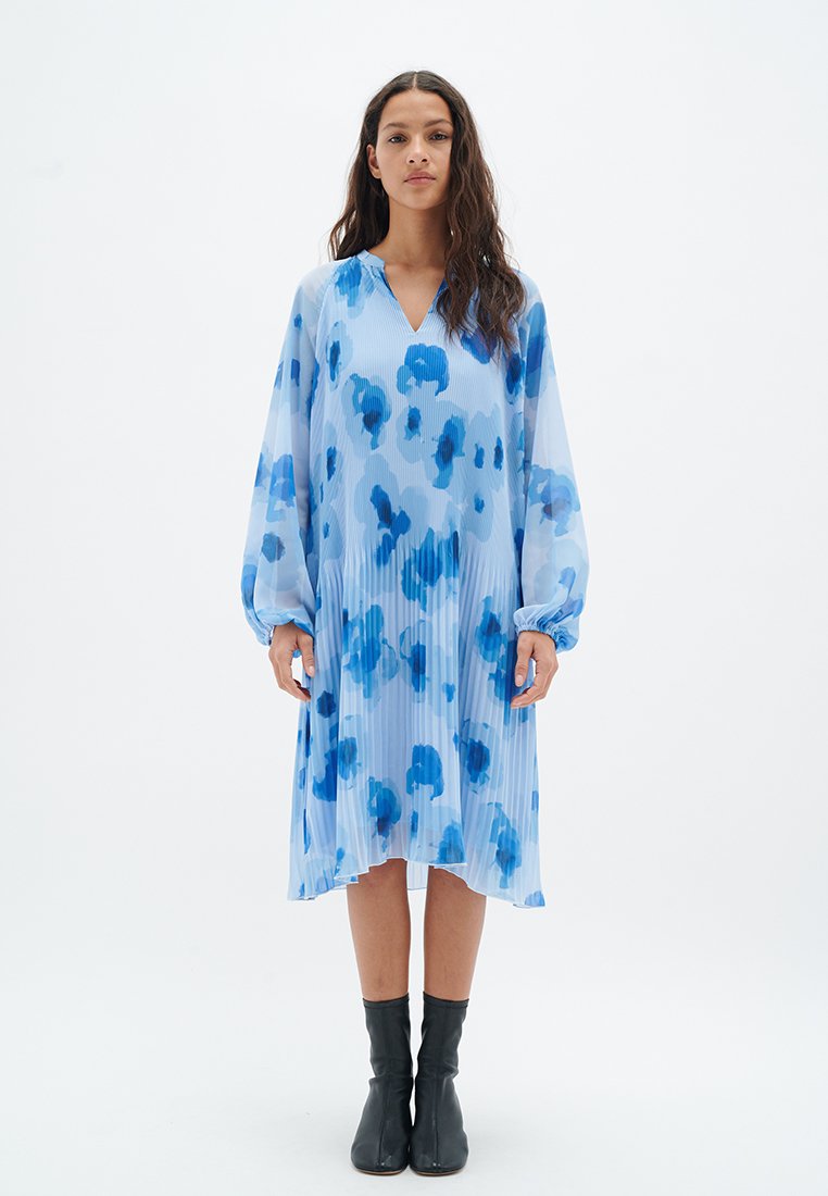 Hellblaues Kleid mit plissierter Optik, das blaue abstrahierte Muster aufweist. Lange Ärmel mit elastischen Bündchen und V-Ausschnitt. Knöchellang.