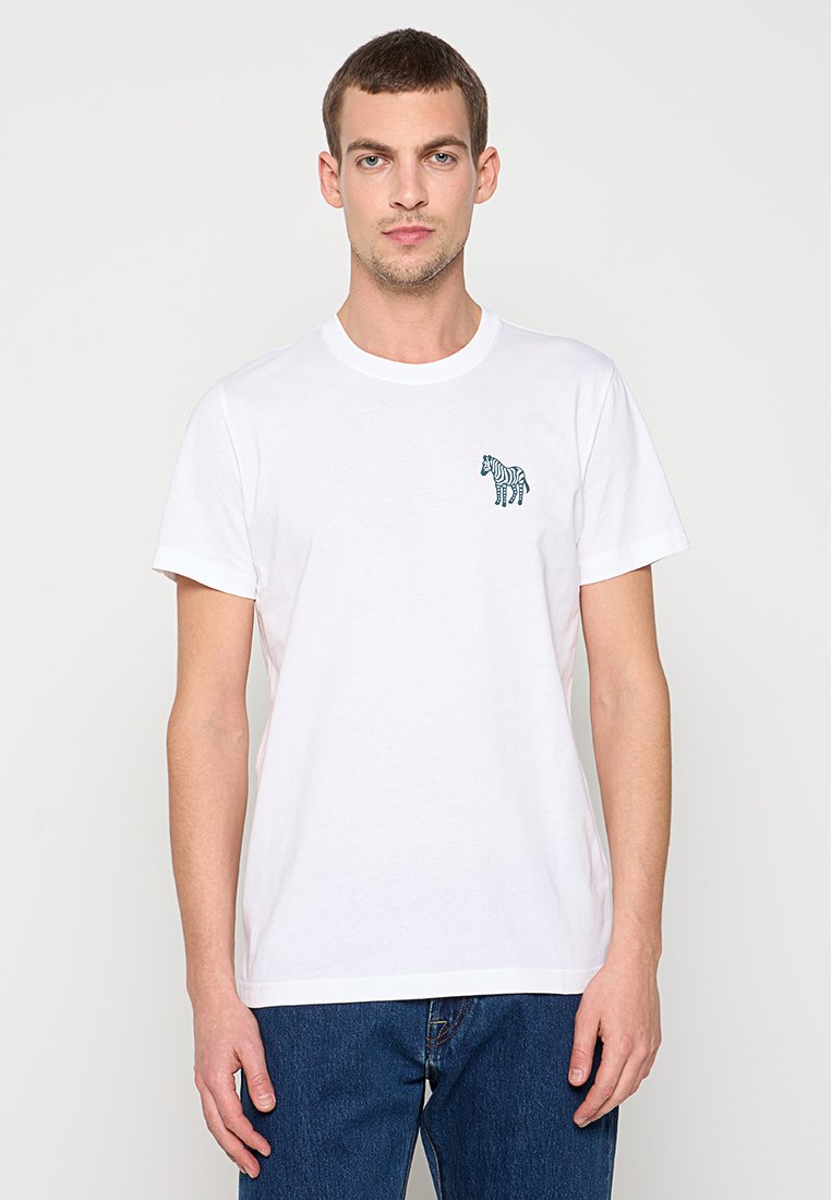 Weißes Baumwoll-T-Shirt mit kleinem grünem Zebra-Aufdruck auf der linken Brust, rundem Halsausschnitt und kurzen Ärmeln, kombiniert mit blauen Jeans.