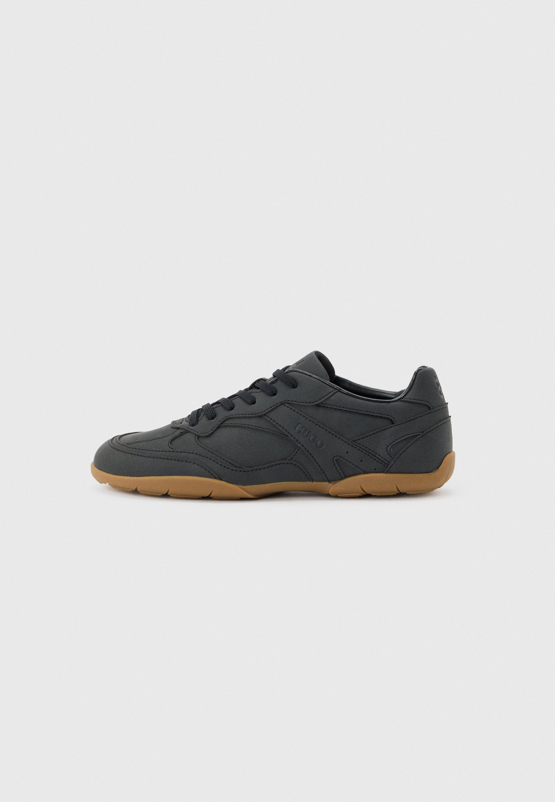 Schwarzer Sneaker mit niedrigem Profil, beigefarbener Gummisohle, seitlichen Schnürsenkeln und dezentem geprägtem Markennamen an der Seite, vor einfarbigem Hintergrund.