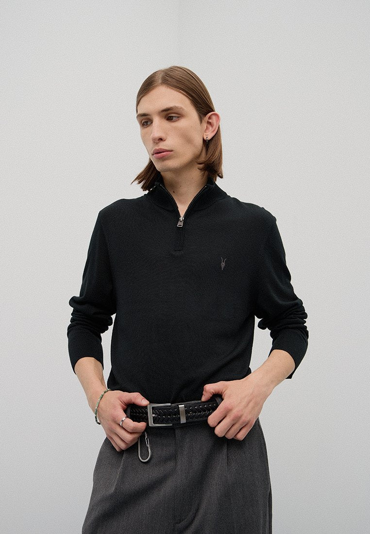 Schwarzer Langarm-Half-Zip-Pullover mit einem dezenten Logo, kombiniert mit grauen, taillierten Hose und einem gewebten schwarzen Gürtel. Glatte Textur, figurnahes Design.