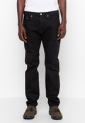 Schwarze Jeans aus Denim mit geradem Schnitt, fünf Taschen-Design, vorderem Knopfverschluss und silbernen Details. Getragen mit dunkelbraunen Schuhen.