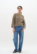 Olivgrüner Strickpullover mit einem lockeren, strukturierten Design, kombiniert mit hellblauen weit geschnittenen Jeans und schwarzen Sandalen.