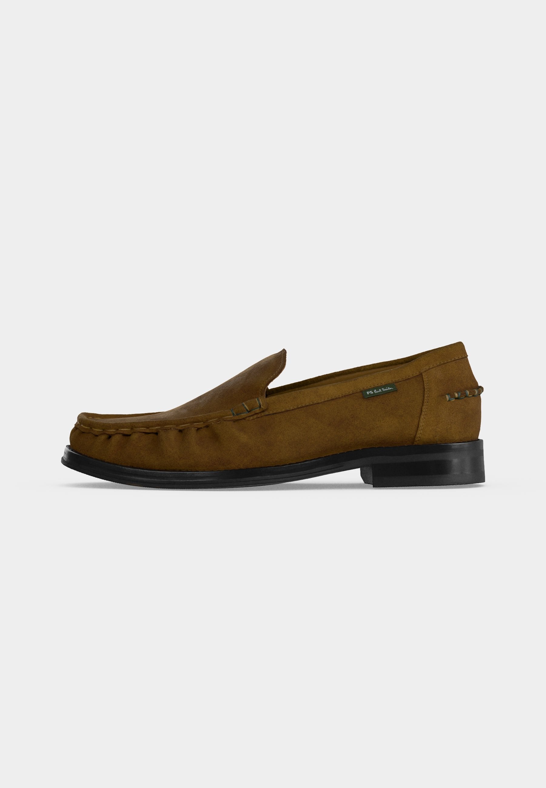 Brauner Velours-Herrenloafer mit schwarzer Sohle, Mokassin-Nähten und kleinem Stoffetikett an der Seite, vor weißem Hintergrund dargestellt.