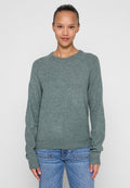Hellgrüner, gestrickter Pullover mit rundem Ausschnitt und gerippten Bündchen, mit langen Ärmeln und lockerer Passform. Kombiniert mit blauen Jeans.