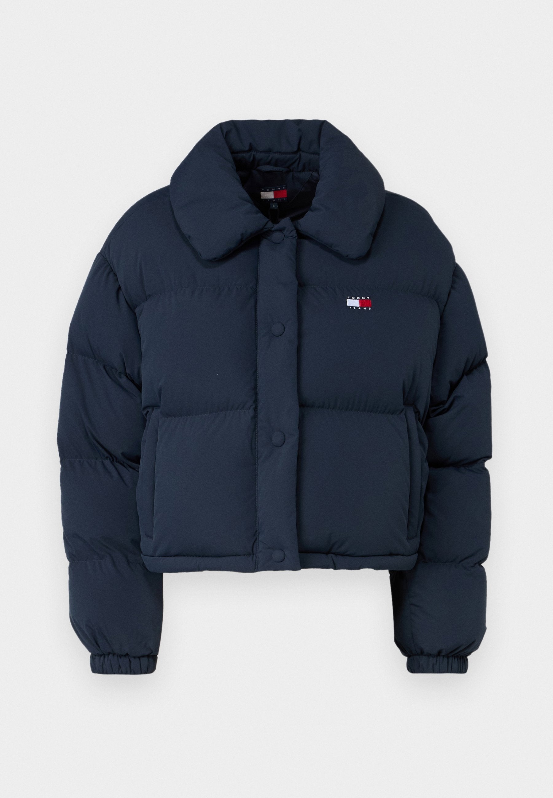Marineblaue Steppjacke mit einem cropped Design, ausgestattet mit einem großen Kragen, Frontknöpfen und einem kleinen Logo mit roten und weißen Akzenten auf der Brust.