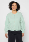 Minzgrüner Cardigan mit rundem Ausschnitt, Knöpfen vorne und weiten Ärmeln. Hergestellt aus weichem, strukturiertem Material, kombiniert mit einer dunklen Jeans.