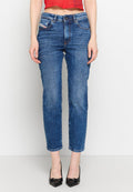Frau in hoch taillierten blauen Jeans, rotem cropped Top und schwarzen spitzen High Heels, stehend vor einem weißen Hintergrund.