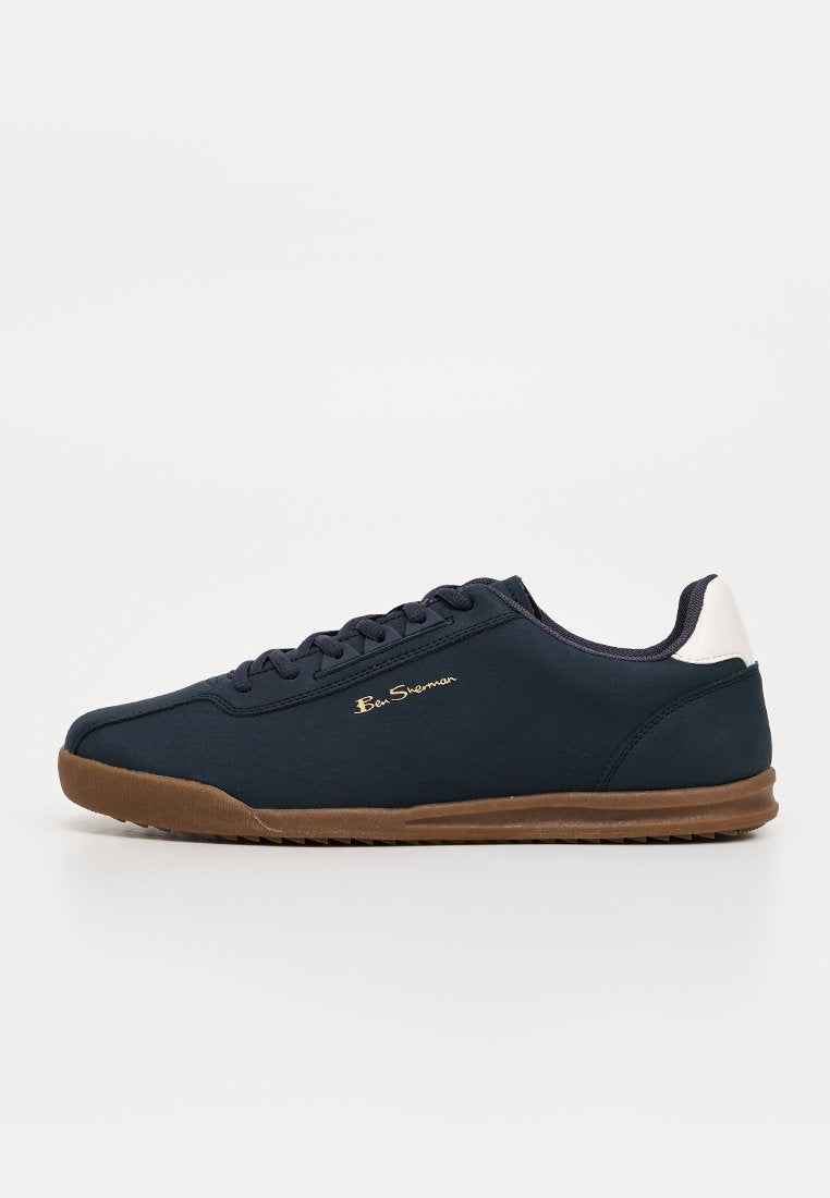 Marineblauer Low-Top-Sneaker mit brauner Sohle, weißem Fersenpatch, Schnürsenkeln und goldenem "Ben Sherman" Logo an der Seite, auf weißem Hintergrund dargestellt.