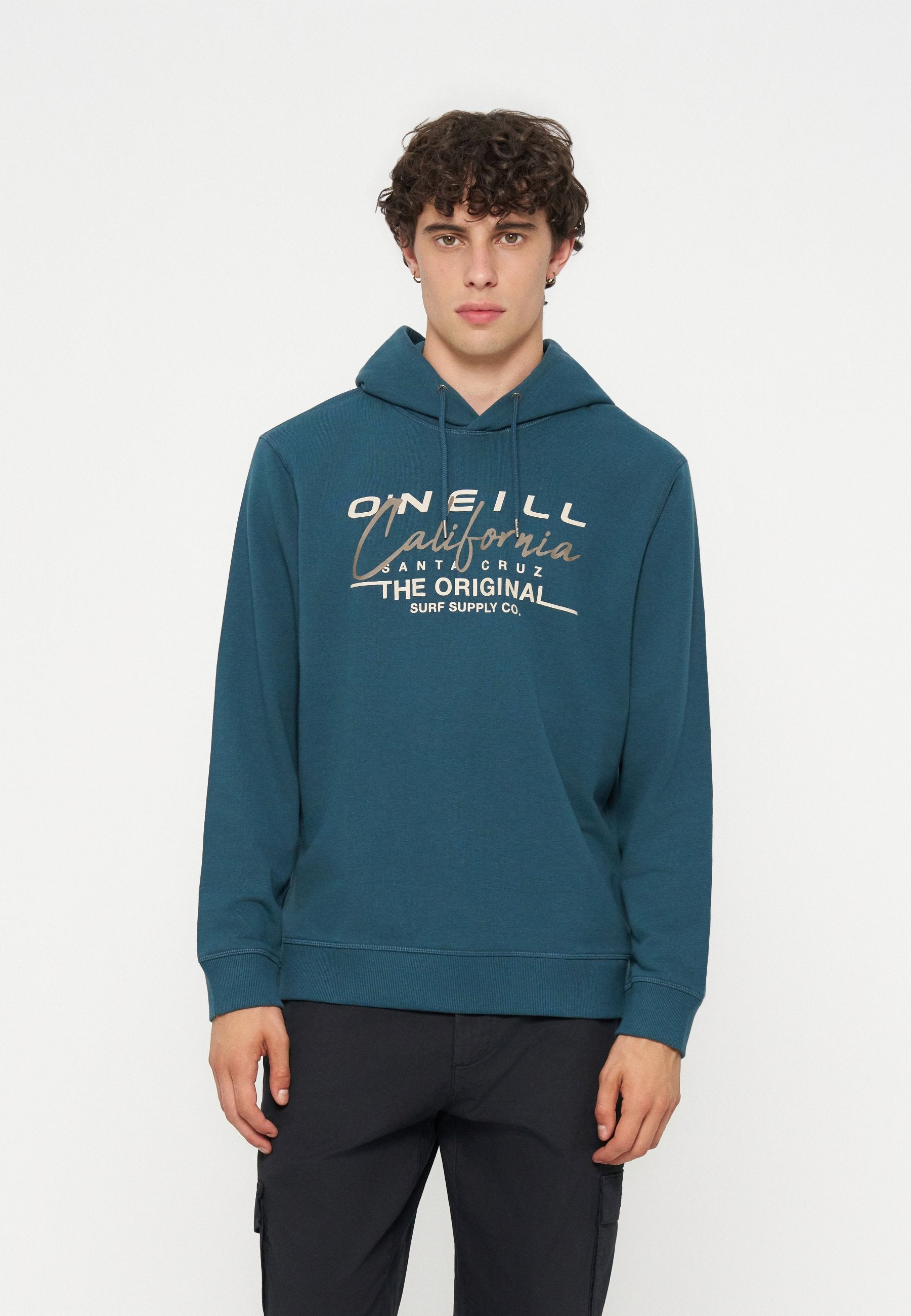 Junger Mann mit lockigem Haar trägt einen türkisfarbenen O'Neill-Hoodie mit dem Schriftzug California Santa Cruz und schwarze Hose, steht vor einem weißen Hintergrund.