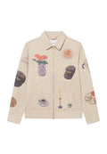Beige Canvas-Jacke mit verschiedenen künstlerischen Drucken, darunter Blumen, Lebensmittel und Haushaltsgegenstände. Reißverschluss vorne und zwei Fronttaschen.