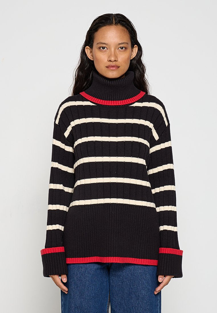 Schwarz-weißer gestreifter Rollkragenpullover mit gerippter Textur, roten Akzenten am Kragen und an den Bündchen sowie lockerem Schnitt.