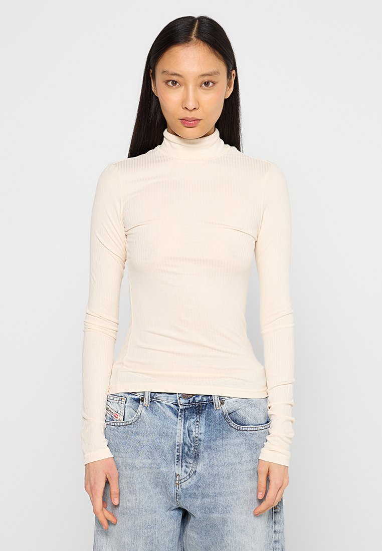 Langärmliges Rollkragenoberteil aus leichtem, strukturiertem Creme-Stoff, mit einer figurbetonten Silhouette und glatter Textur, kombiniert mit hochtaillierten blauen Jeans.