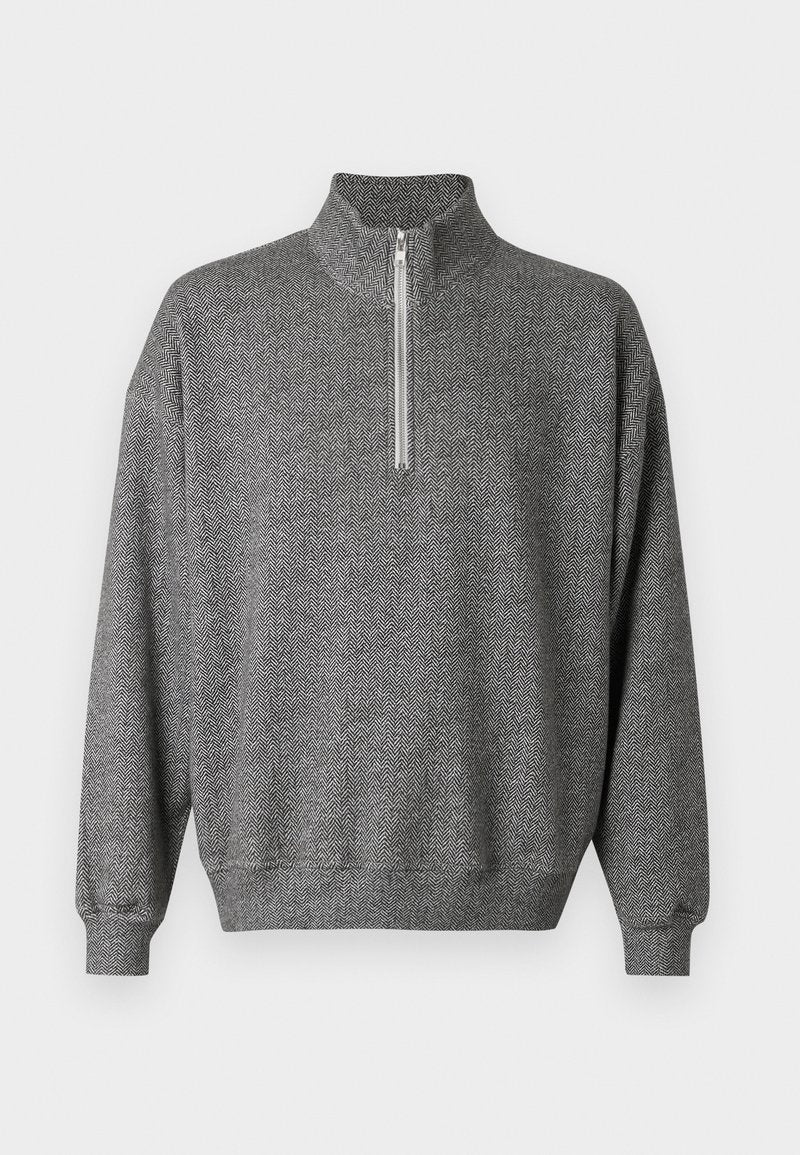 Grauer Herringbone-Pullover mit hohem Kragen und Viertel-Reißverschluss. Ausgestattet mit gerippten Bündchen und Saum, die eine strukturierte Optik verleihen.