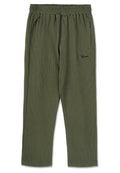 Olivgrüne gerippte Hose mit elastischem Bund, Seitentaschen und einem kleinen schwarzen Logo auf der Vorderseite. Der Stoff hat eine strukturierte Oberfläche.