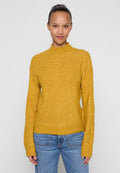 Senfgelber Strickpullover mit hohem Kragen, langen Ärmeln und legerer Passform, kombiniert mit hellblauen Jeans.