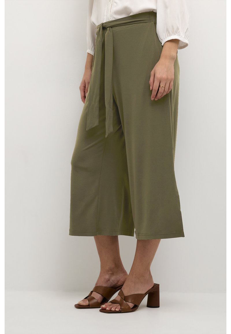 Olivengrüne, weit geschnittene Hose mit einem Taillenknoten. Aus weichem Stoff gefertigt und mit einer glatten Textur versehen. Kombiniert mit braunen Blockabsatzsandalen.
