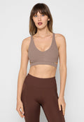 Sport-Bra aus hellbraunem Rippstoff mit tiefem V-Ausschnitt, breiten Trägern und einem Unterbrustband. Kombiniert mit hoch taillierten braunen Leggings.