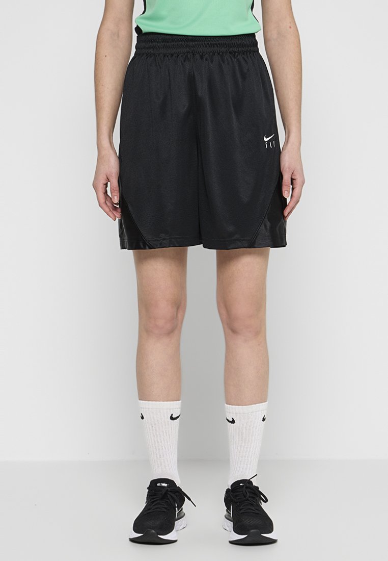 Schwarze Sportshorts mit elastischem Bund, die eine glatte Textur und seitliche Akzente aufweisen. Kombiniert mit weißen Socken und schwarzen Turnschuhen.