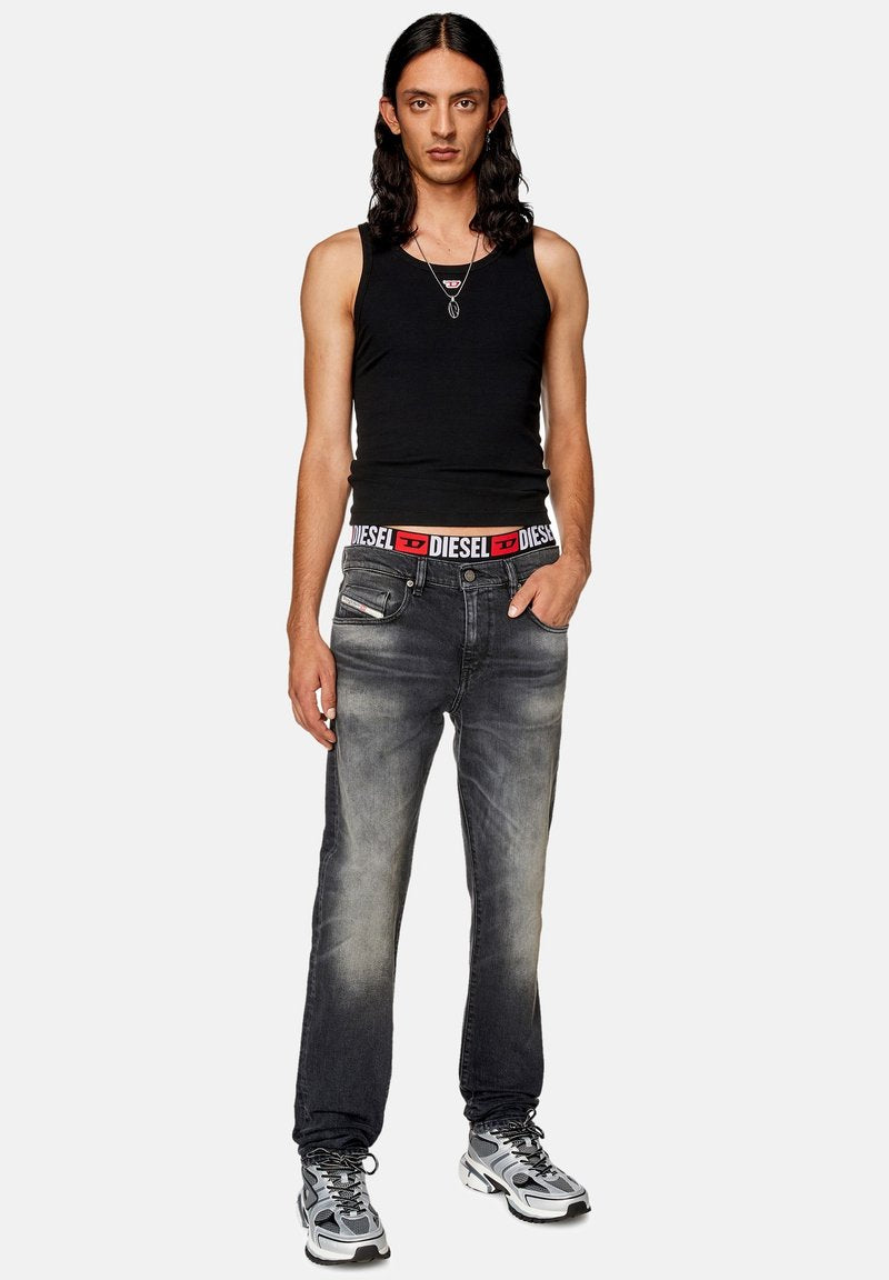 Schwarzes Tanktop, dunkelgraue Denim-Jeans mit ausgewaschenem Finish, auffälliges Diesel-Logo am Bund und graue Sneaker mit Mesh-Design.