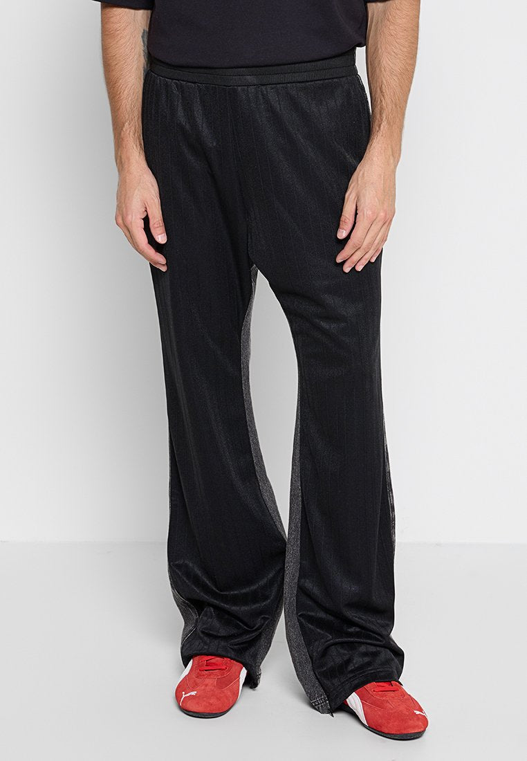 Schwarze Sporthose mit einem Streifenmuster, elastischem Bund und schmal zulaufenden Beinen. Kombiniert mit roten Sportschuhen.