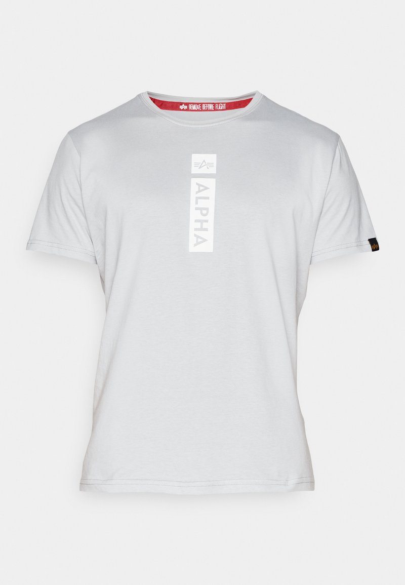 Graues Baumwoll-T-Shirt mit einem vertikalen "ALPHA"-Logo in Weiß auf der Vorderseite, einem runden Halsausschnitt und einem roten Etikett innen mit "REMOVE BEFORE FLIGHT."