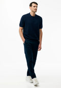 Mann trägt ein marineblaues, strukturiertes Poloshirt mit kurzen Ärmeln, dunkle Hose und weiße Sneakers, geht mit einer Hand in der Tasche.