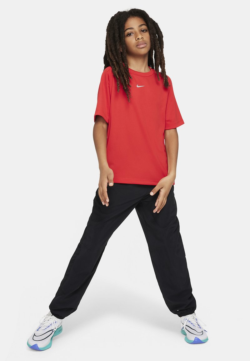 Rotes Kurzarm-Sportshirt mit einem kleinen weißen Logo, kombiniert mit schwarzen, locker sitzenden Hosen und weißen Sneakers mit türkisfarbenen Akzenten.