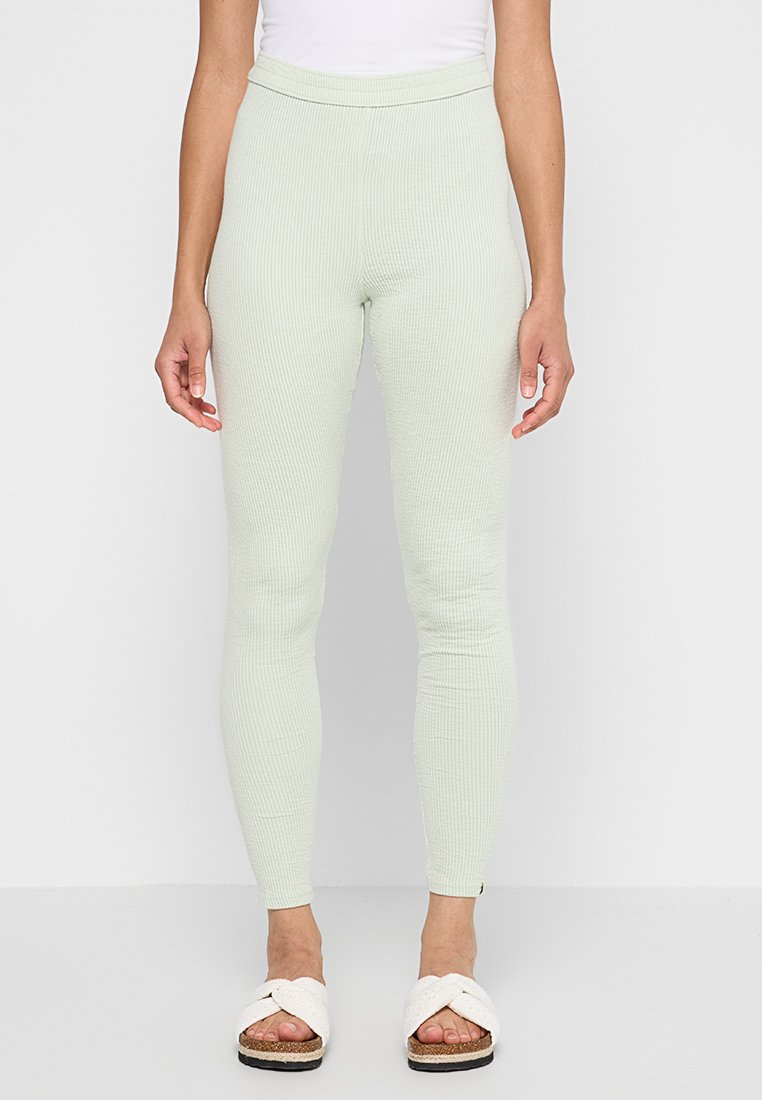 Helle grüne, gerippte Leggings mit hohem Taillenbund und enger Passform. Strukturierter Stoff; Modell trägt ein weißes Oberteil und helle Sandalen.