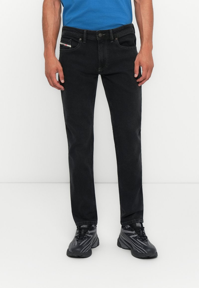 Schwarze Jeans im geraden Schnitt mit fünf Taschen, kontrastierenden Nähten und einem Markenetikett an der Vordertasche. Kombiniert mit schwarzen Schuhen.