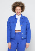 Blaue Jeansjacke mit klassischem Kragen, Fronttaschen und silbernen Knopfakzenten, kombiniert mit einem weißen Crop-Shirt und passenden blauen Hosen.