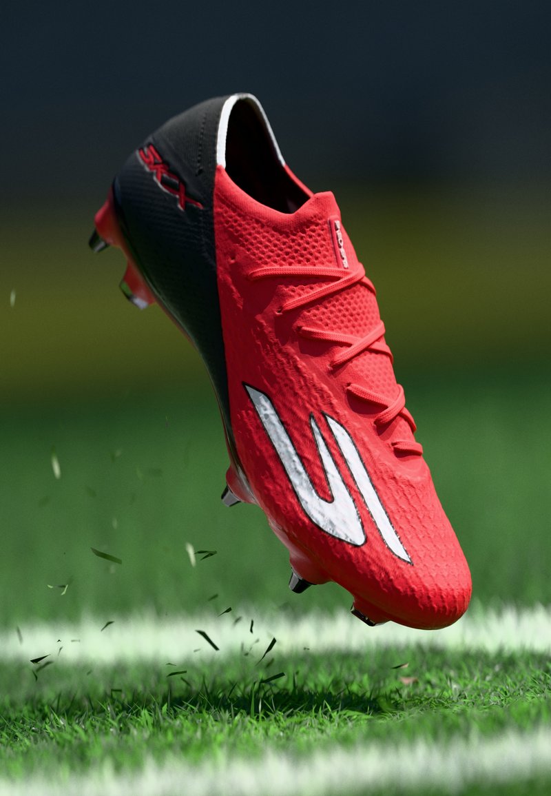 Roter und schwarzer Fußballschuh mit weißem Logo, in der Luft über einem Grasfeld mit aufgewirbeltem Rasen und sichtbarer weißer Begrenzungslinie.