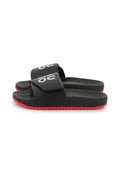 Schwarze Rutsch-Sandalen mit einem strukturierten Riemen, der ein auffälliges weißes Logo zeigt. Rote Gummisohle mit einem Zickzackmuster für besseren Halt.