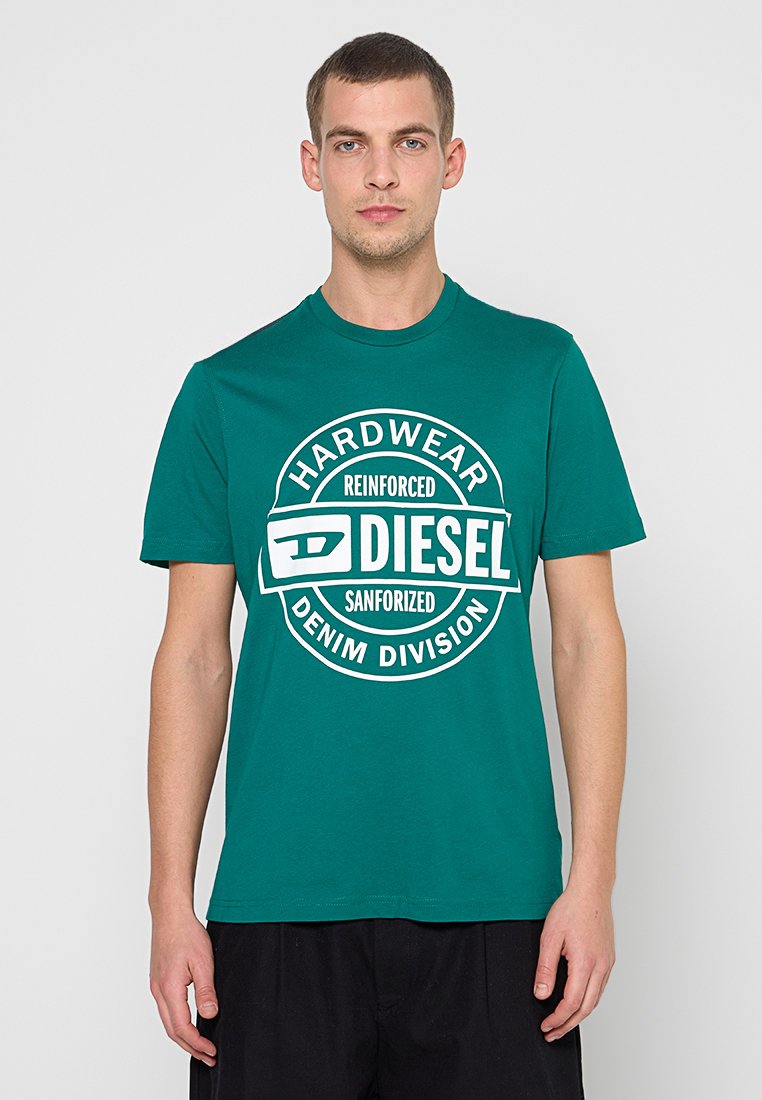 Grünes Baumwoll-T-Shirt mit kurzen Ärmeln, das ein rundes weißes Grafiklogo mit dem Text „HARDWEAR REINFORCED SANFORIZED DENIM DIVISION“ zeigt.