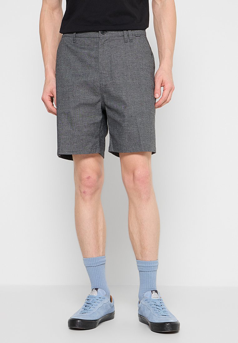 Grau karierten Shorts mit einem klassischen Schnitt, die seitliche Taschen, einen Knopfverschluss und eine glatte Stoffoberfläche bietet. Getragen mit hellblauen Turnschuhen.