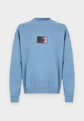 Hellblauer Pullover mit langen Ärmeln, geripptem Kragen, Bündchen und Saum, mit einem mittig angebrachten schwarzen rechteckigen Aufnäher mit der Aufschrift "HUGO".