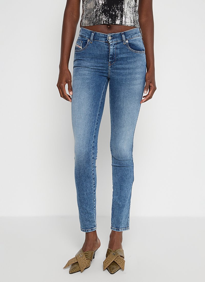 Schmale blaue Jeans, getragen von einer Person mit abgeschnittenen Schlangenleder-Fersen mit Riemen und einem kurzärmligen Oberteil mit schwarz-weißer Musterung.