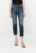 Frau in dunkelblauen, cropped Denim-Jeans und schwarzen, geschlossenen High Heels, die vor einem weißen Hintergrund steht.