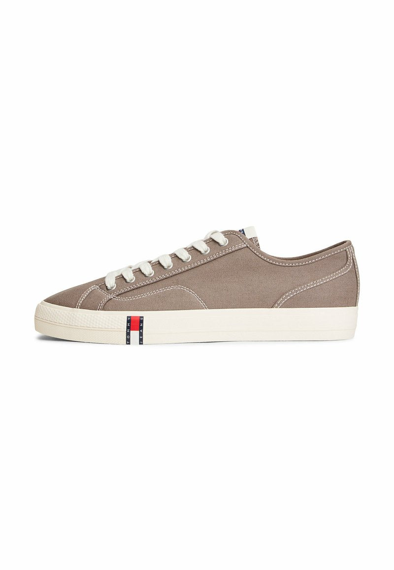 Niedriger Sneaker aus taupefarbenem Segeltuch mit weißen Schnürsenkeln, weißer Gummisohle und einem kleinen rot-weiß-blauen Logo an der Seite.