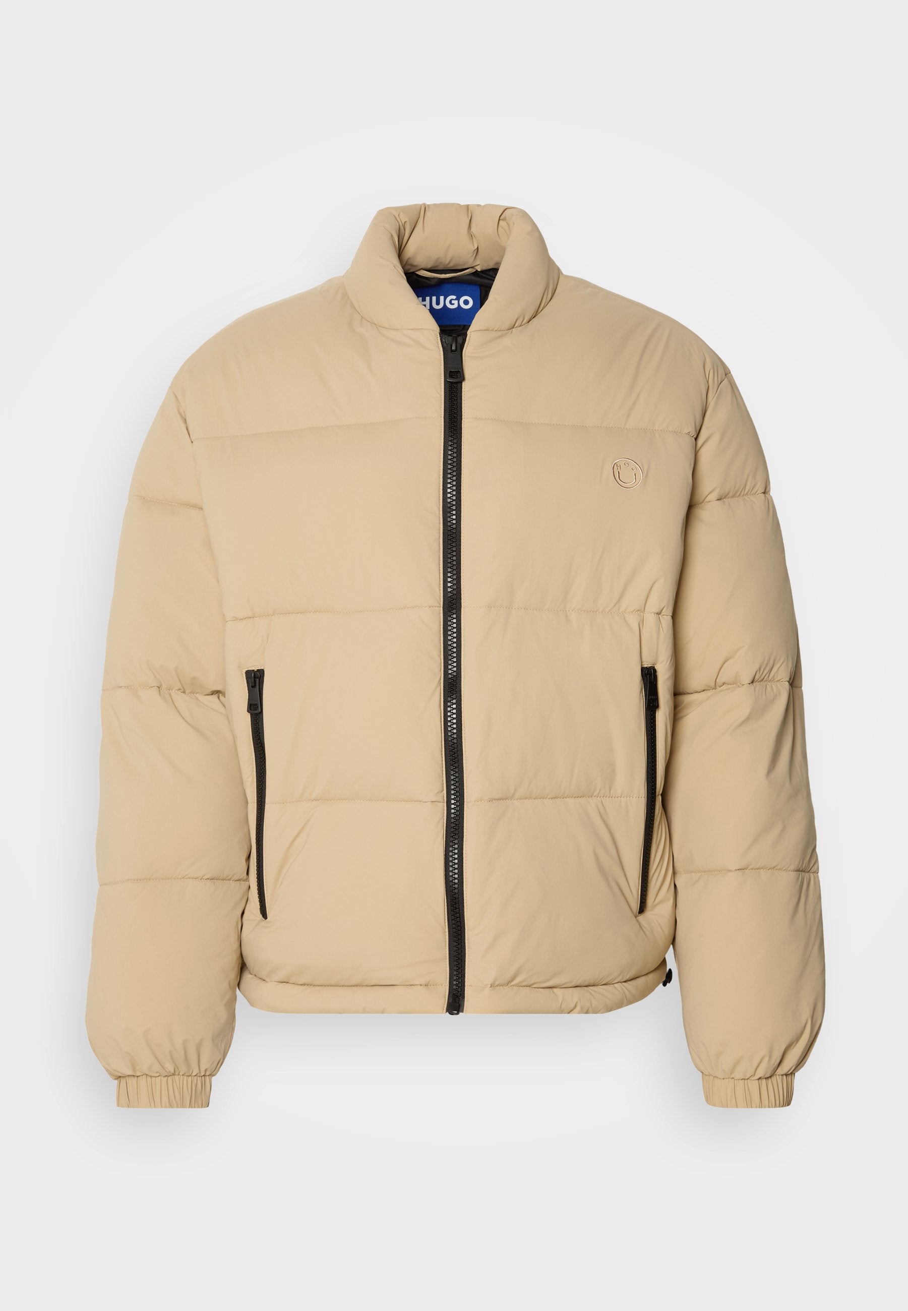 Beige Daunenjacke mit hohem Kragen, Reißverschluss vorne und zwei Reißverschlusstaschen. Mit gestepptem Muster und elastischen Bündchen. Logo auf der Brust.
