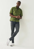 Olivegrühe Kurzarmhemd mit zwei Brusttaschen, kombiniert mit dunkelgrauen Slim-Fit-Jeans und weißen Sneakers.