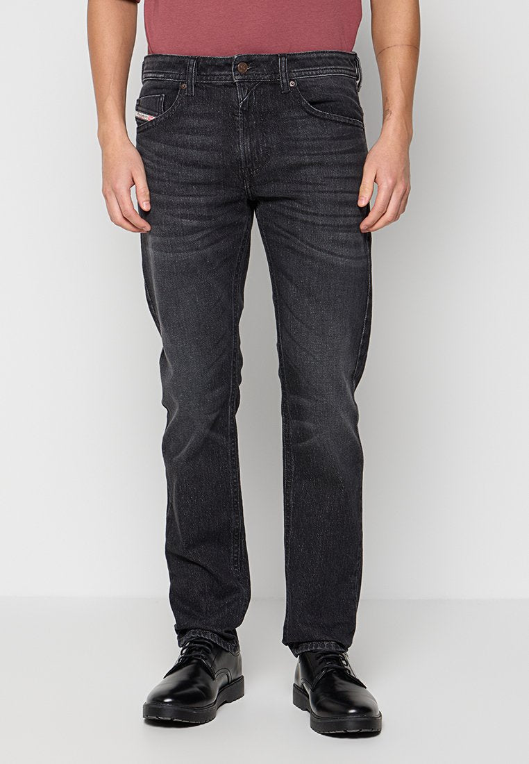 Schwarze Denim-Jeans für Herren mit geradem Bein, fünf Taschen und kontrastierender Naht. Getragen mit schwarzen eleganten Schuhen und einem burgunderroten Hemd.