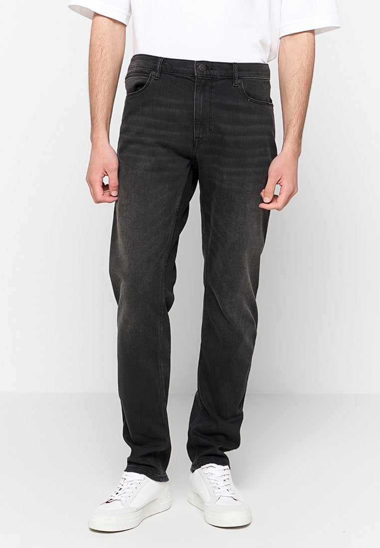 Schwarze Denim-Jeans mit geradem Bein, versehen mit verblassten Akzenten und klassischem Fünf-Taschen-Design. Eingerahmt mit weißen Sneakern.