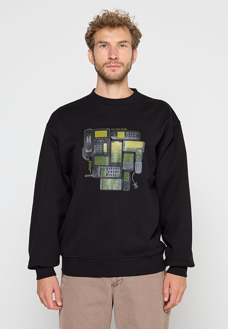 Mann trägt einen schwarzen Sweatshirt mit einer Grafik von verschiedenen Vintage- und modernen Mobiltelefonen in grünen und grauen Farbtönen.