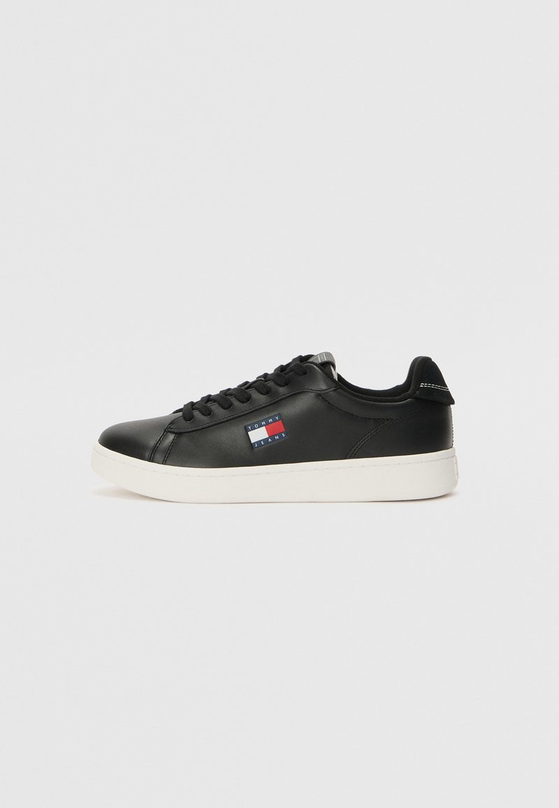 Schwarze Ledersneaker mit weißer Gummisohle, versehen mit einem Logo-Label in Rot, Weiß und Blau an der Seite und flachen schwarzen Schnürsenkeln.