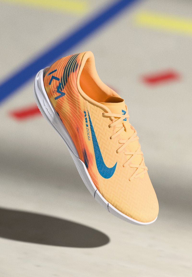 Der Nike Sportschuh verfügt über ein leichtes oranges Obermaterial mit blauen Akzenten, einem strukturierten Muster, einer Schnürung und einer weißen Sohle.