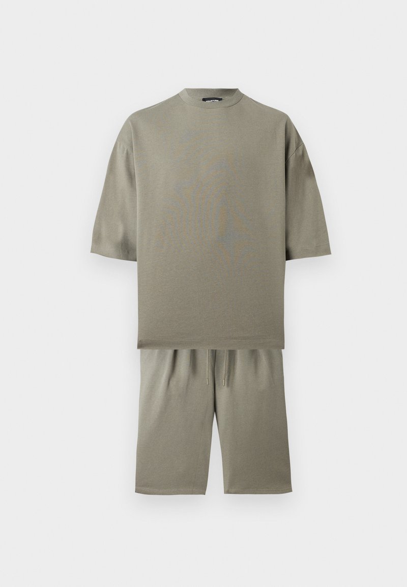 Beiges Oversize-T-Shirt mit kurzen Ärmeln, kombiniert mit beige knielangen Shorts vor weißem Hintergrund.