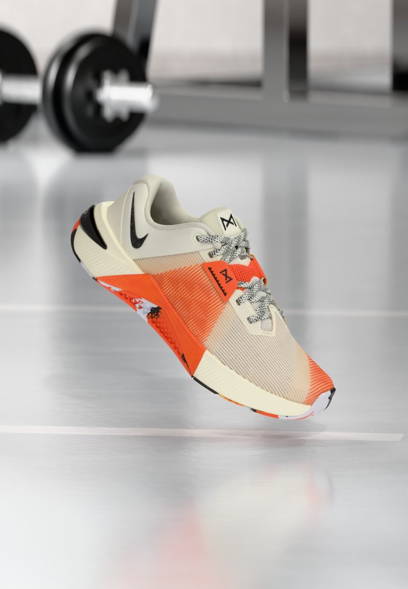 Leichte Sportschuhe in Creme, Orange und Schwarz. Sie verfügen über ein strukturiertes Obermaterial, ein schwarzes Swoosh-Logo und eine gemusterte Sohle für besseren Grip.