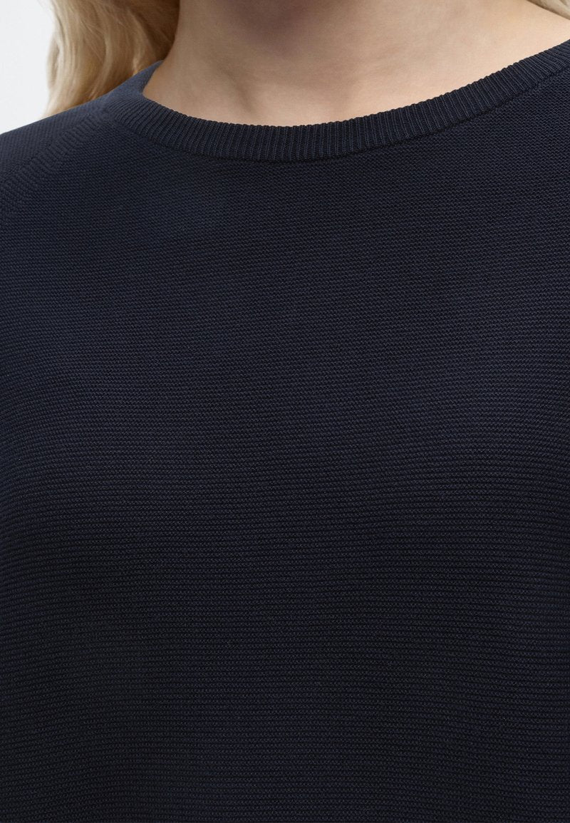 Nahaufnahme einer Person, die einen dunkel marineblauen, strukturierten Strickpullover mit rundem Ausschnitt trägt, wobei ein Teil des Halses und der oberen Brust sichtbar ist.